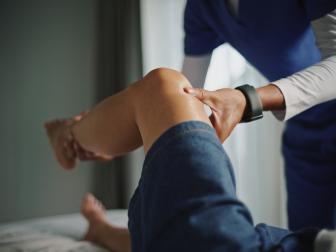 Physiotherapeut untersucht und mobilisiert das Knie einer Patientin.