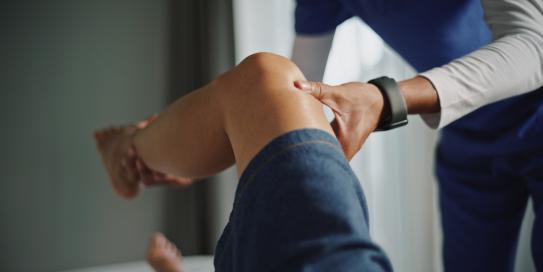 Physiotherapeut untersucht und mobilisiert das Knie einer Patientin.