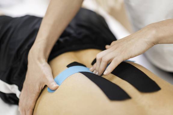Physiotherapeut bringt Kinesiotape am Rücken eines Patienten an